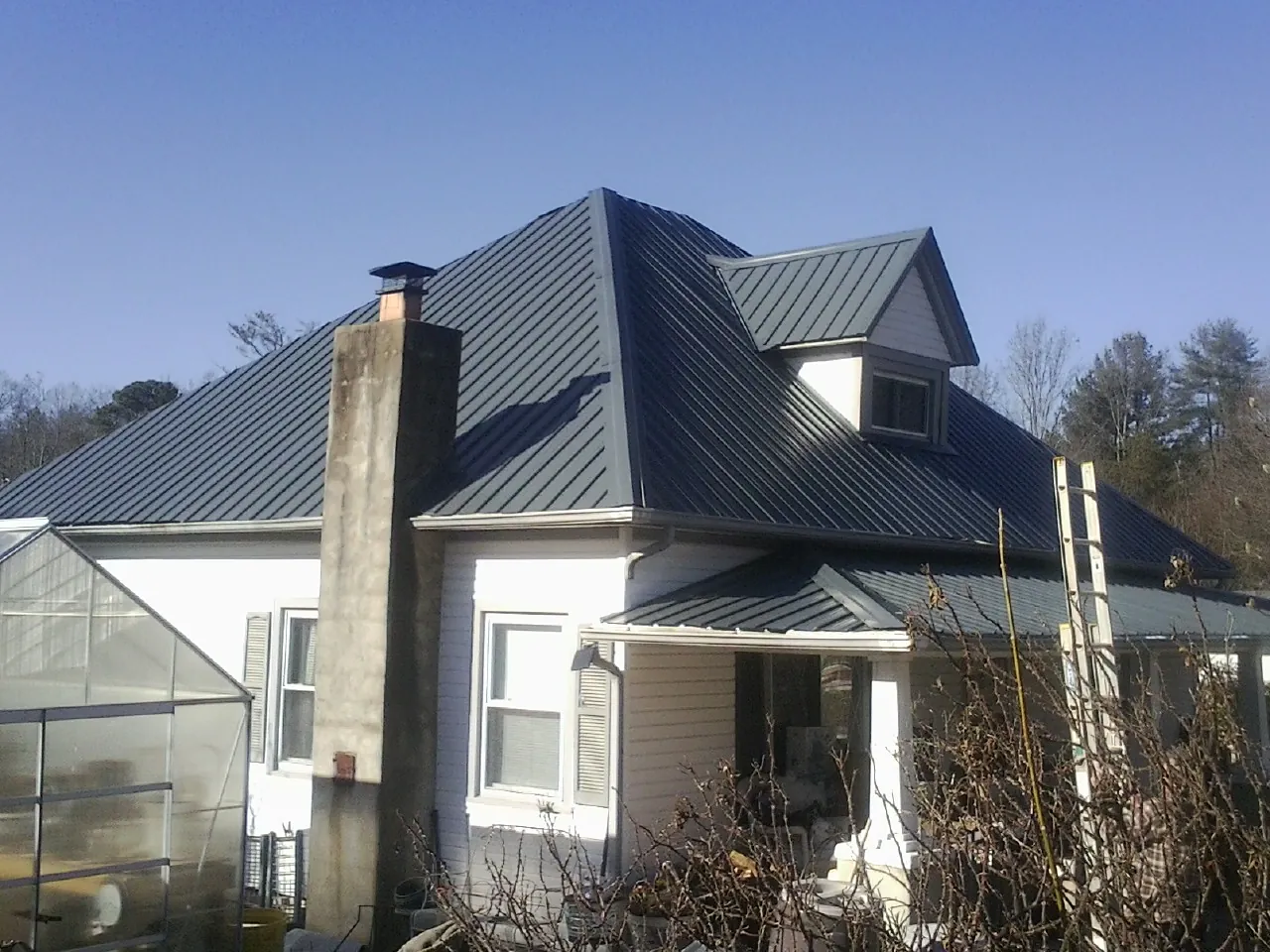 Dark blue standing seam metal roof on a white farmhouse with dormer — Slate & Tile Roof Repair by Roofing Brothers in Rossburg