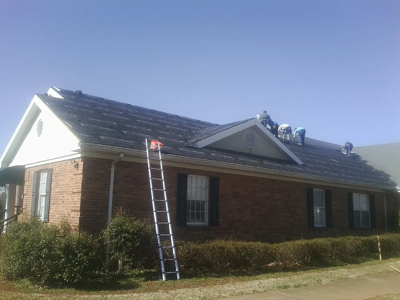 Crew tearing shingles off a brick ranch roof with a ladder set — Metal Roof Repair work by our crew in Rossburg