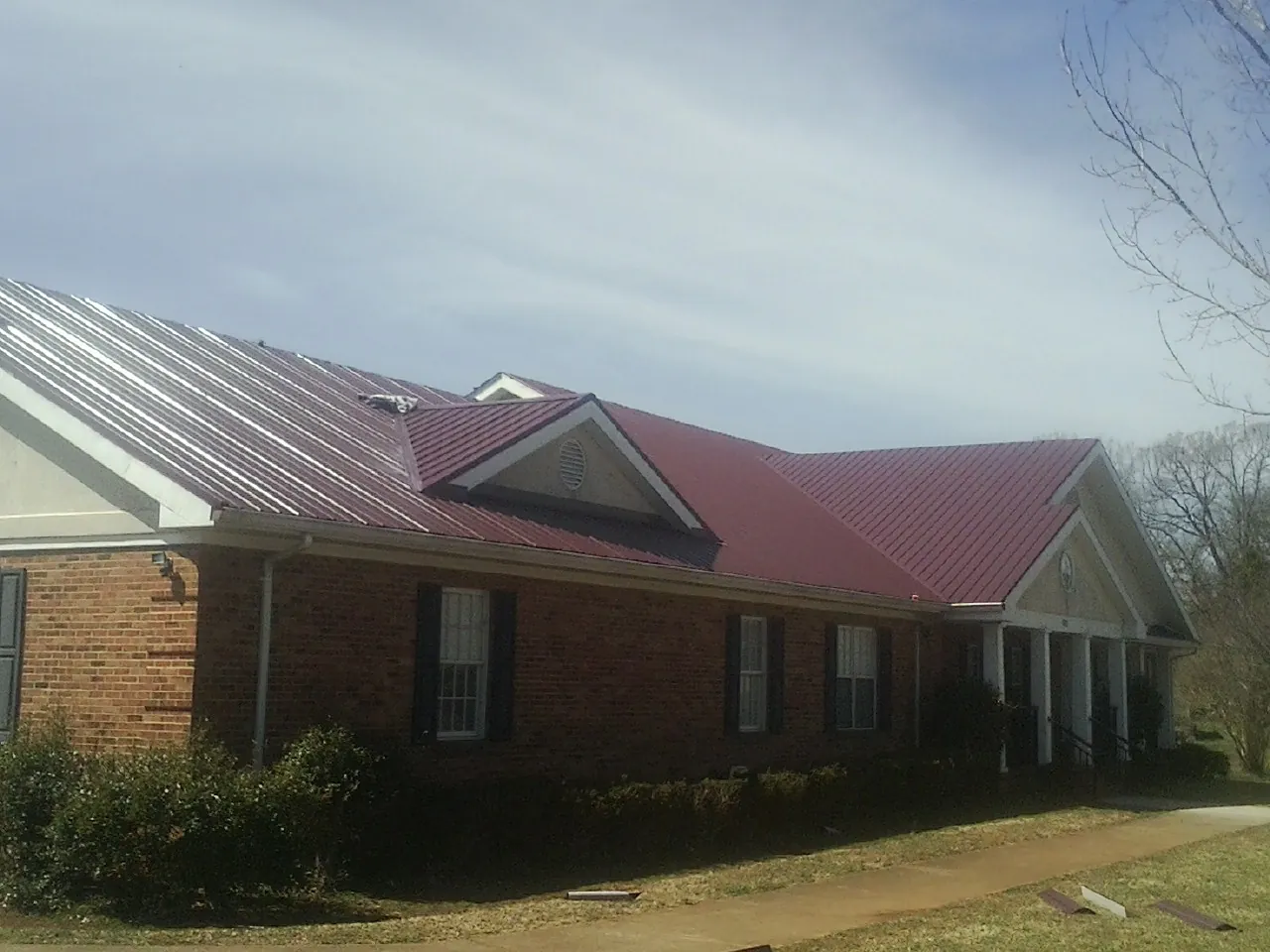 Red metal roof with gabled entries on a long brick building, from a Hail Damage Roof Repair job in Rossburg