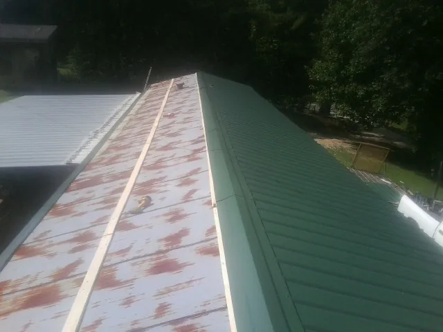 Old rusted panels beside newly installed green metal roofing — Wind Damage Roof Repair by Roofing Brothers in Rossburg