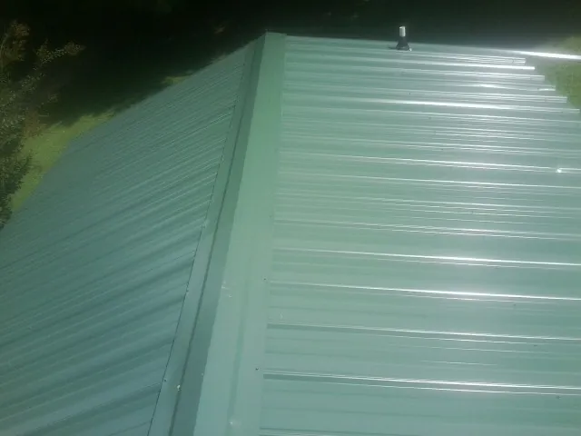 New green metal panels meeting at the ridge of a roof — Flat Roof Repair work by our crew in Rossburg