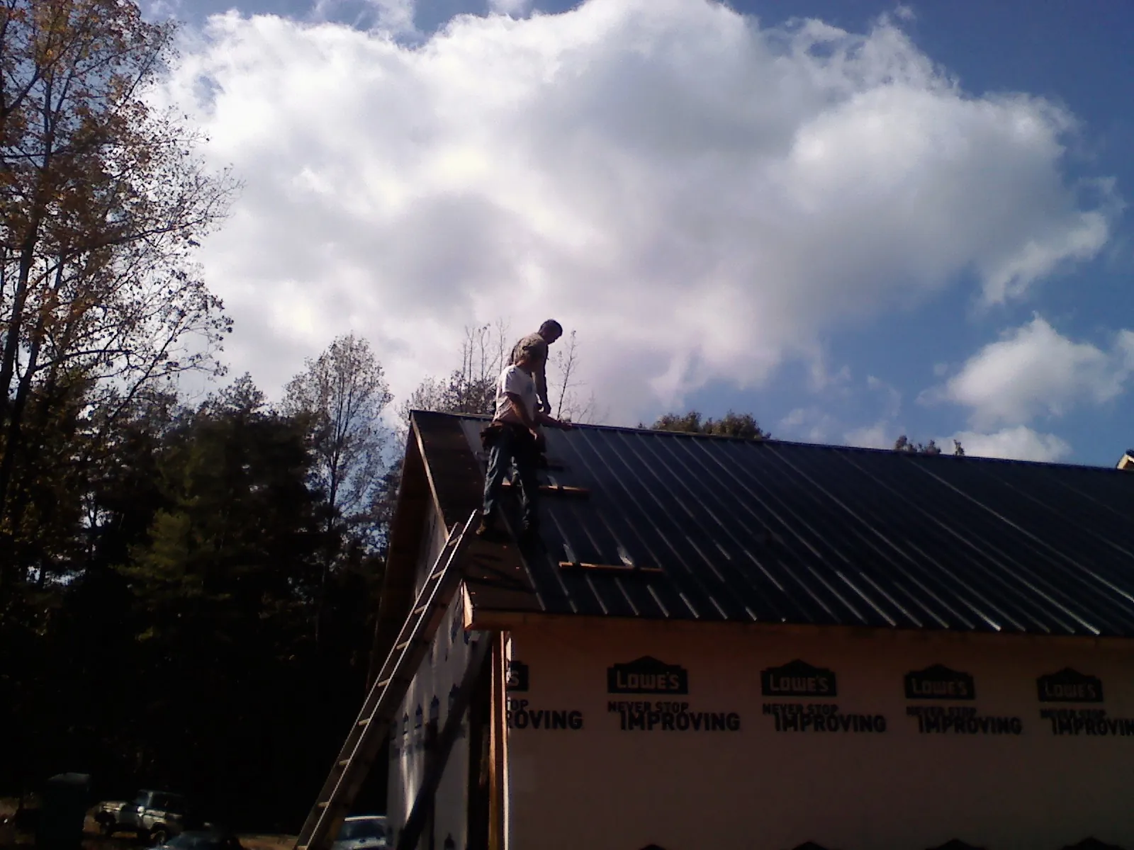 Roofer fastening dark metal panels high against a cloudy sky, from a Roof Inspection job in Rossburg