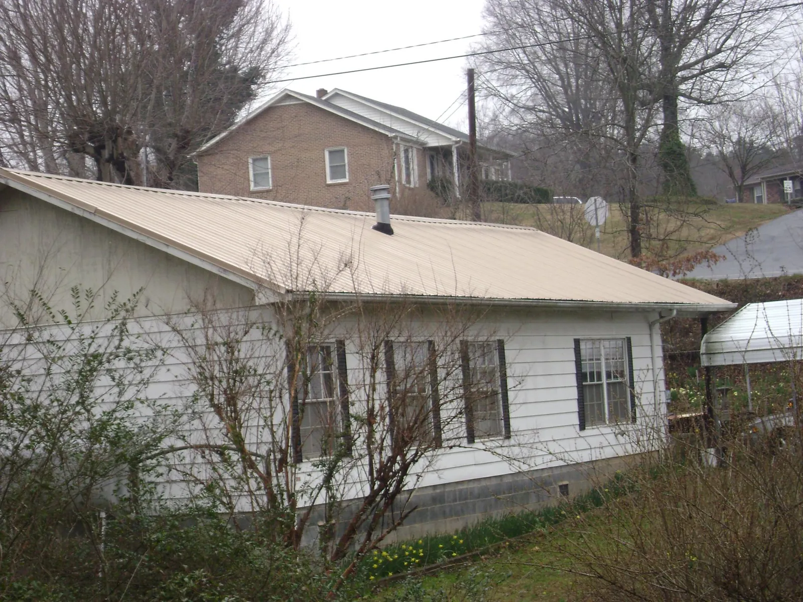 Tan metal roof on a white sided house set into a hillside — Commercial Roofing by Roofing Brothers in Rossburg